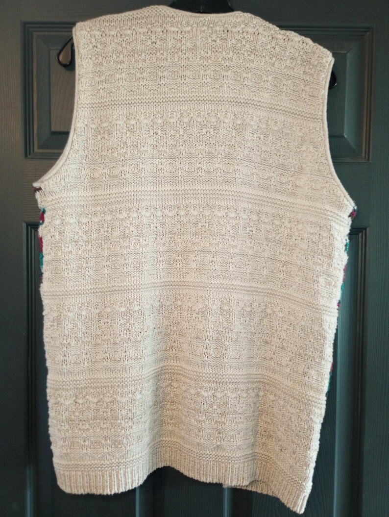 May include: A cream-colored knitted vest with a textured pattern. The vest has a V-neck and sleeveless design.