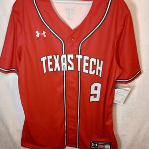 以下が含まれることがあります： 胸元に白い文字でTexas Tech、白い数字の9、襟と前立てに沿った黒と白のパイピング、胸にUnder Armourのロゴがあしらわれた、赤い半袖のボタンダウン野球用ジャージ。