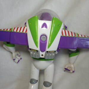 May include: A plastic action figure of a space ranger character featuring a white, purple, and lime green color scheme. The figure has a clear dome helmet, extendable purple wings with red and white striped accents, and labels reading DANGER and JET EXHAUST.