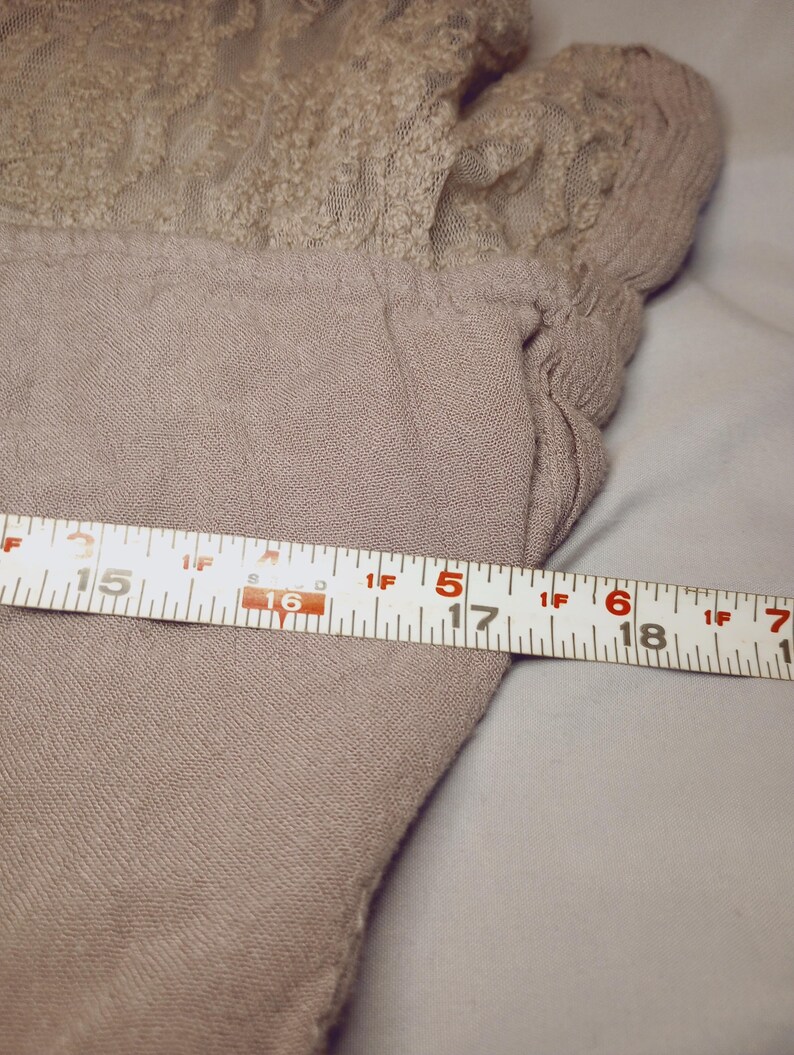 May include: A light brown garment with a lace detail at the top. The garment is measured with a tape measure, showing a width of approximately 17 inches.