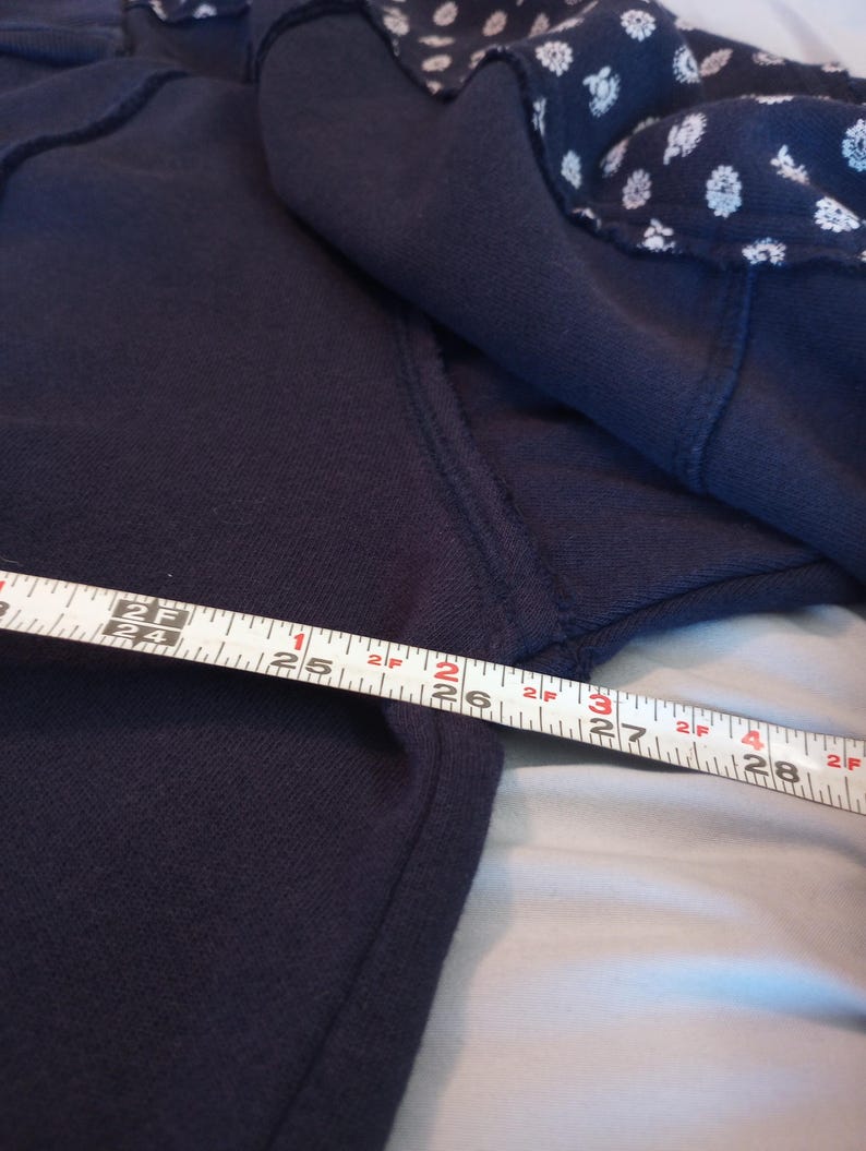 May include: Navy blue sweatshirt with a white floral pattern on the shoulder. The tape measure shows a length of approximately 26 inches.