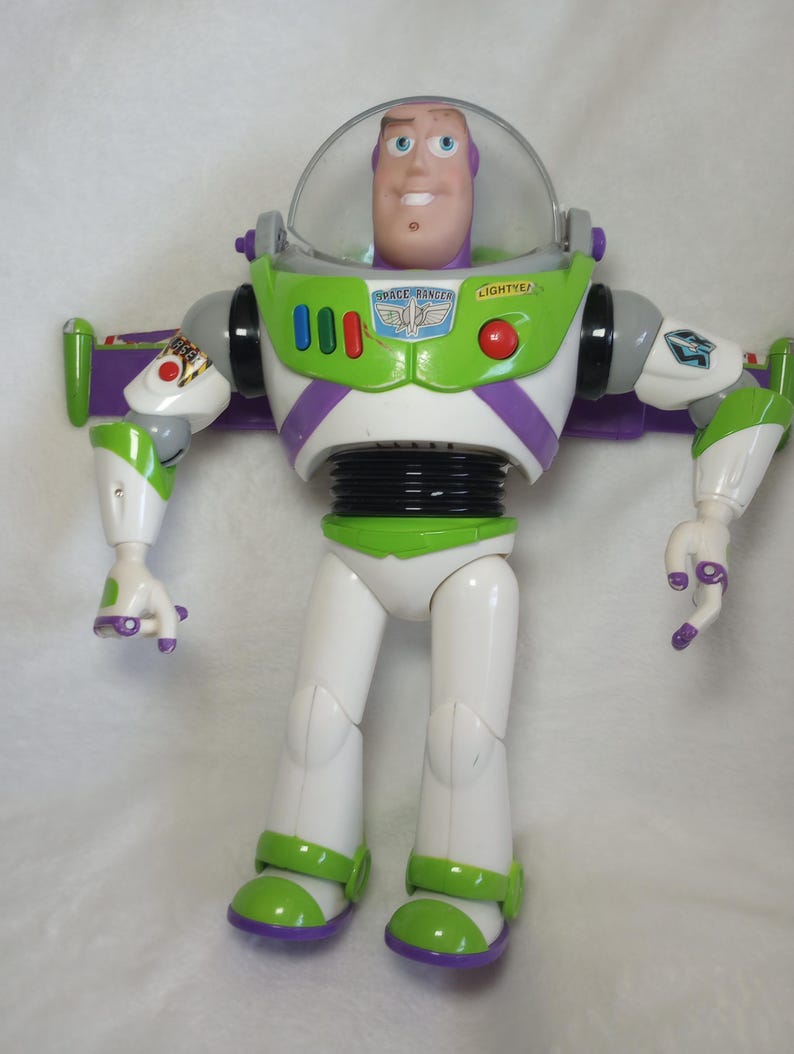 May include: A Buzz Lightyear action figure featuring a white, lime green, and purple plastic suit with a clear retractable helmet. The chest displays the text SPACE RANGER and LIGHTYEAR with a blue and silver emblem, three red buttons, and a red circular button.