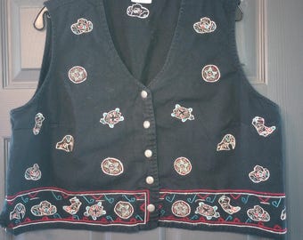 Puede incluir: Chaleco vaquero negro con diseños bordados de estilo suroeste. El chaleco presenta un cuello en V, cierre de botones y parches decorativos de sombreros, botas y patrones geométricos. El dobladillo inferior tiene un borde rojo y turquesa.