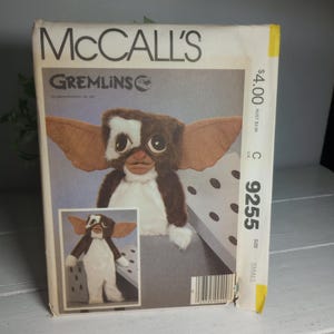 以下が含まれることがあります： グレムリンのキャラクターのヴィンテージMcCall'sソーイングパターン。パターンは、大きな耳、茶色と白の毛皮、および「Gremlins」のテキストを備えたグレムリンキャラクターのカラーイラストを特徴としています。 パターン番号は9255です。