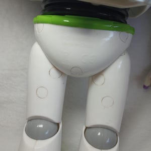 May include: A plastic action figure torso and legs featuring a white hip section with a bright green waist trim, white upper legs, and grey knee joints. The white hip area displays molded text reading Disney Pixar and Made in China.