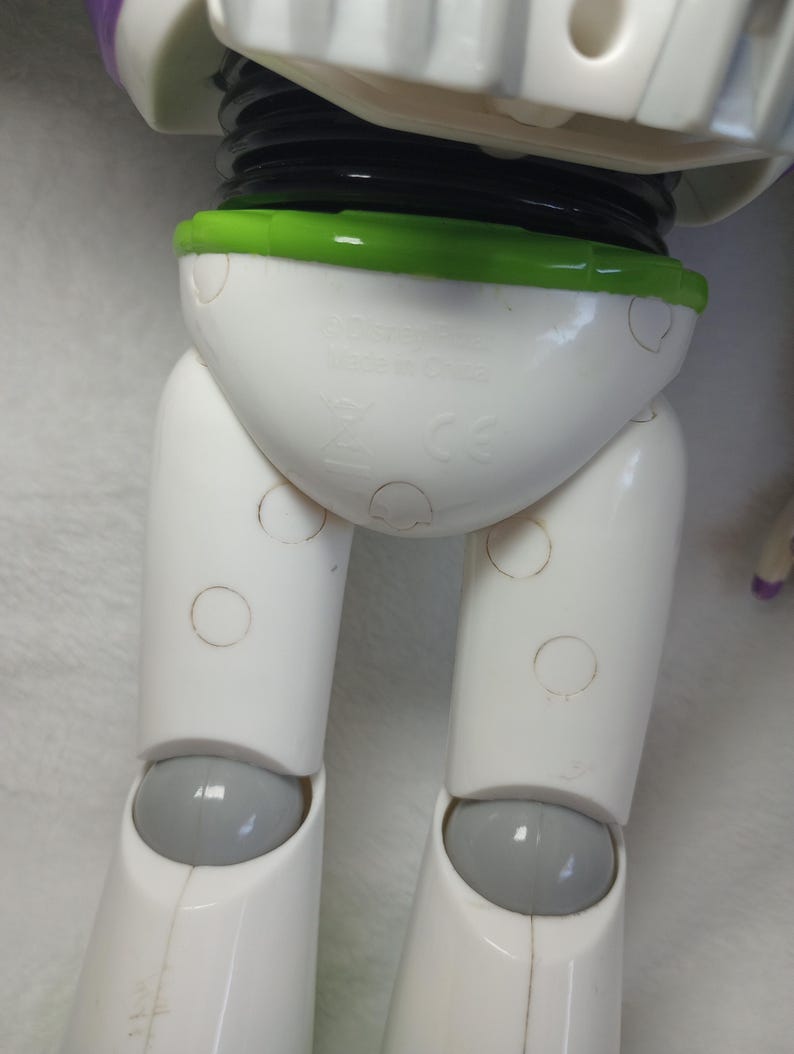 May include: A plastic action figure torso and legs featuring a white hip section with a bright green waist trim, white upper legs, and grey knee joints. The white hip area displays molded text reading Disney Pixar and Made in China.