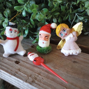 May include: A selection of vintage Christmas decorations, featuring a snowman with a red scarf, Santa Claus, an angel with gold wings, and a Santa Claus tree topper. The ornaments are made of felt and plastic.