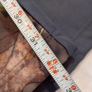 Puede incluir: Primer plano de tela gris con detalle de estampado de camuflaje. Una cinta m&eacute;trica muestra la longitud de la tela, con marcas de 74 a 84 cm. La tela tiene una apariencia texturizada.