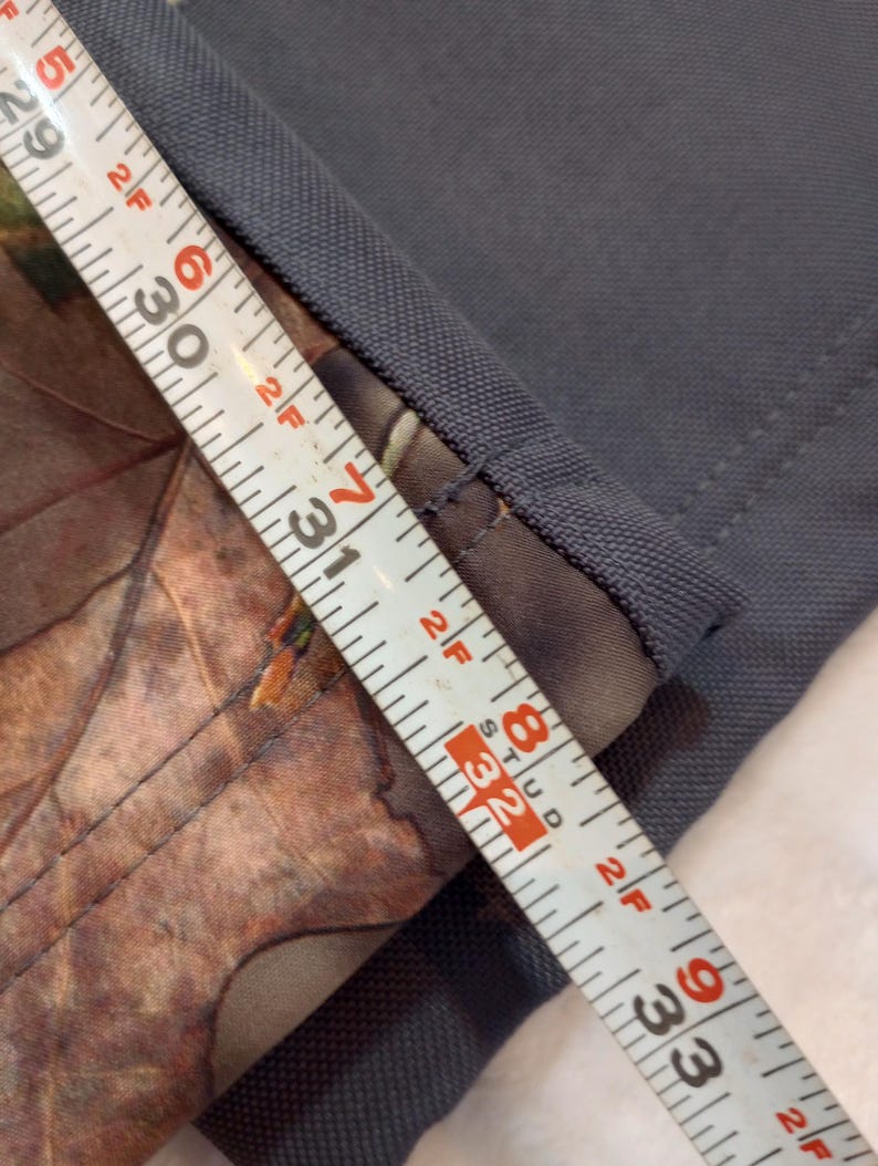 Puede incluir: Primer plano de tela gris con detalle de estampado de camuflaje. Una cinta m&eacute;trica muestra la longitud de la tela, con marcas de 74 a 84 cm. La tela tiene una apariencia texturizada.