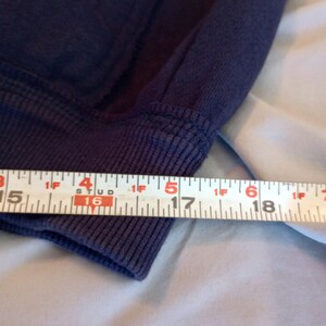 May include: Close-up of a navy blue sweatshirt cuff with a ribbed knit design. A measuring tape shows the cuff is approximately 6 inches wide. The fabric appears soft and slightly worn.
