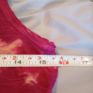 May include: A sleeveless, tie-dye style top in shades of pink and cream. The top is measured with a ruler, showing a width of approximately 35.5 to 43 cm.