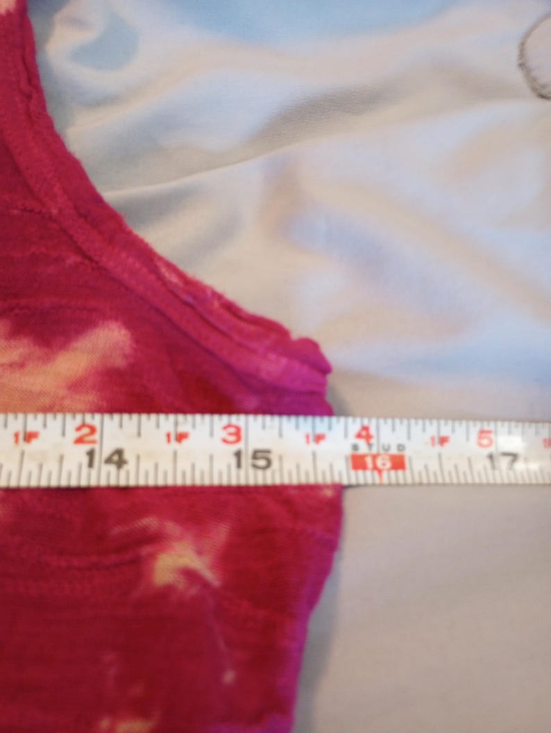 May include: A sleeveless, tie-dye style top in shades of pink and cream. The top is measured with a ruler, showing a width of approximately 35.5 to 43 cm.