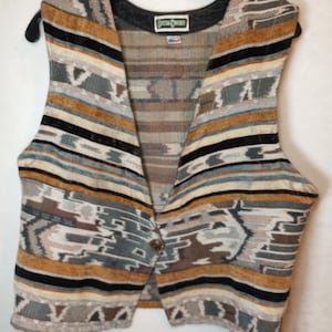 May include: A sleeveless vest featuring a woven tapestry pattern in shades of mustard yellow, black, white, and muted blue-gray. The garment has a single brown button closure at the front and a black collar lining with a label reading Catcha Covered.