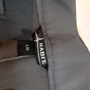 Puede incluir: Primer plano de una prenda gris oscuro con una etiqueta negra. La etiqueta dice "HABIT" en letras may&uacute;sculas blancas con un gr&aacute;fico de latido card&iacute;aco y "L/G" en blanco. La prenda parece estar hecha de un material suave y flexible.