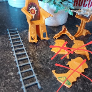 May include: A set of orange plastic toy pieces, including a chair, a ladder, and several other pieces. The pieces are scattered on a gray surface.