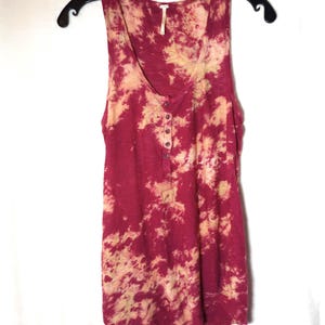 May include: A burgundy and beige tie-dye sleeveless tank top. The top features a scoop neck and a button-up placket. It is displayed on a black hanger against a white backdrop.