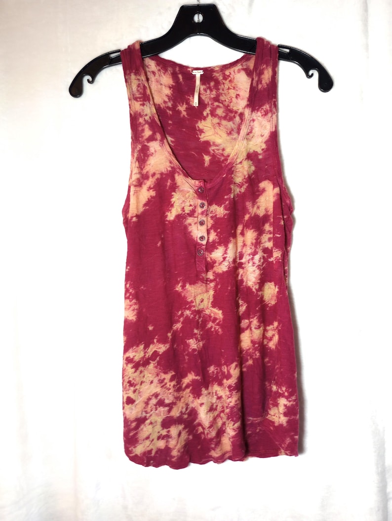 May include: A burgundy and beige tie-dye sleeveless tank top. The top features a scoop neck and a button-up placket. It is displayed on a black hanger against a white backdrop.