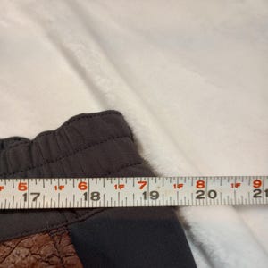 Puede incluir: Primer plano de unos pantalones cortos deportivos de color gris oscuro con un panel marr&oacute;n texturizado. Los pantalones cortos se miden con una regla, mostrando un ancho de aproximadamente 12,7 cm en el panel.