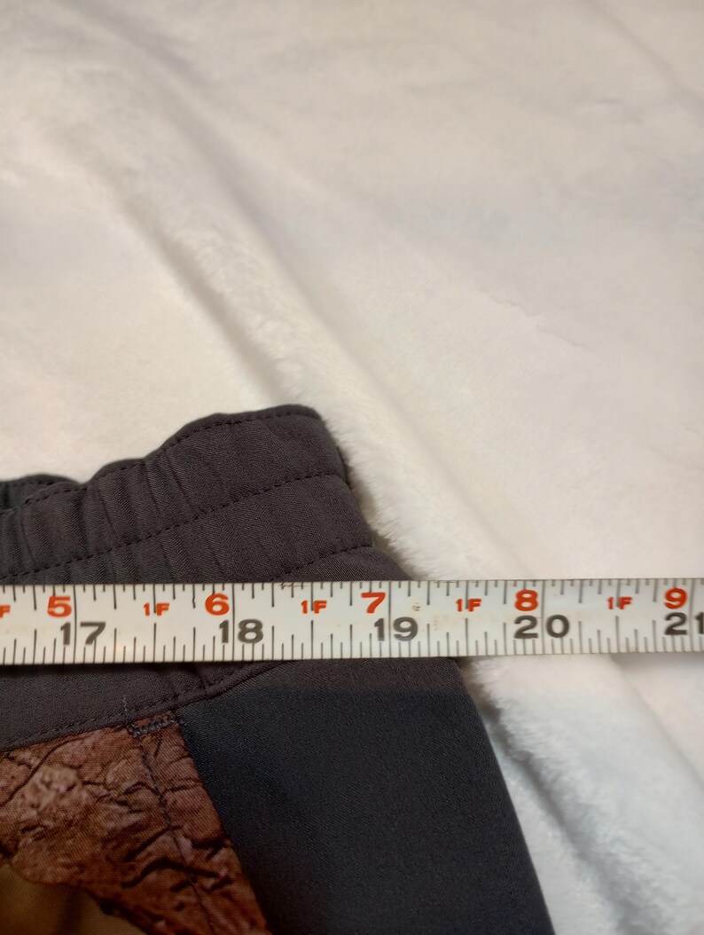 Puede incluir: Primer plano de unos pantalones cortos deportivos de color gris oscuro con un panel marr&oacute;n texturizado. Los pantalones cortos se miden con una regla, mostrando un ancho de aproximadamente 12,7 cm en el panel.