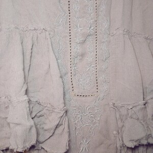 May include: A light gray dress with intricate floral embroidery and ruffled details. The dress features a textured fabric and a delicate, flowing design, perfect for a bohemian or vintage aesthetic.
