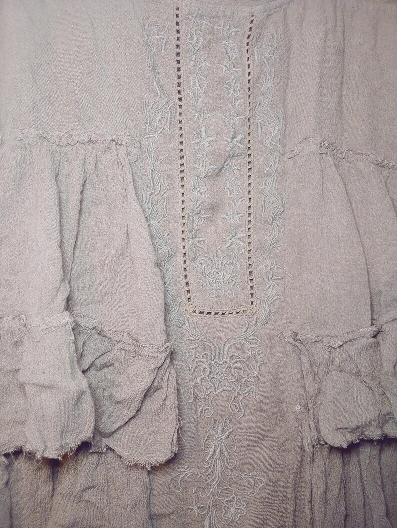 May include: A light gray dress with intricate floral embroidery and ruffled details. The dress features a textured fabric and a delicate, flowing design, perfect for a bohemian or vintage aesthetic.