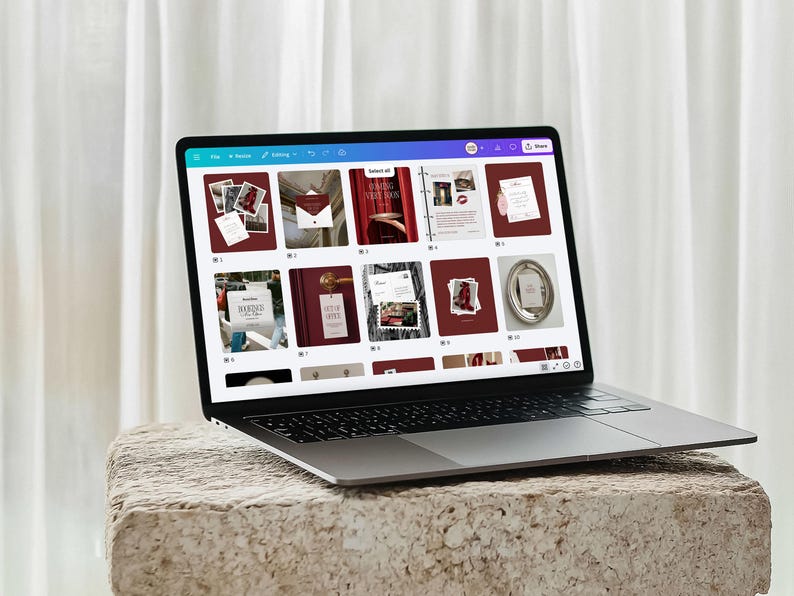 May include: A laptop displaying a website with various design templates. The screen shows a grid of images with a burgundy and white color scheme. The laptop is on a textured, light-colored stone surface.