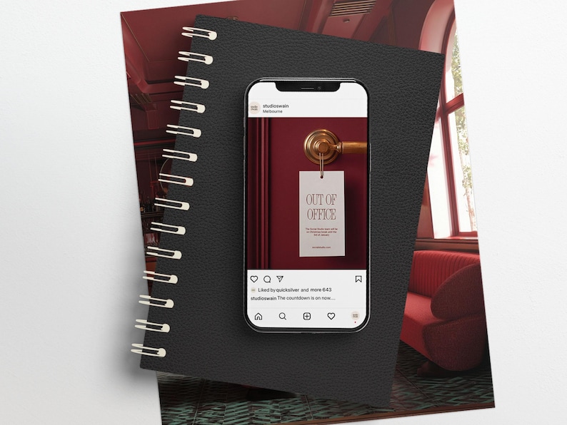 May include: A smartphone displays an "Out of Office" door hanger on a burgundy door. The phone rests on a black spiral-bound notebook. The background includes a red sofa and a window.