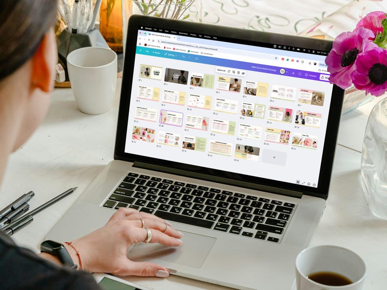 May include: A person using a laptop computer to view a presentation with multiple slides. The slides are colorful and feature text and images. The laptop is on a white table with a cup of coffee and a vase of flowers.