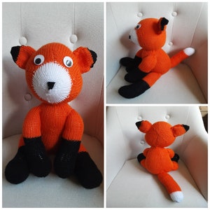 May include: A hand-knitted orange fox plush toy with black legs and white facial details. The fox is sitting on a white armchair.