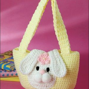May include: A yellow crocheted bunny-shaped bag with a white bunny face and pink flower. The bag has a long yellow strap.