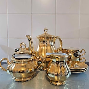 May include: A complete gold tea set, comprising a teapot, sugar bowl, creamer jug, and several teacups with saucers. The set has a shiny, reflective surface and ornate handles, suggesting a vintage or luxury design.
