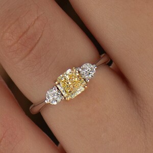 K&ouml;nnte beinhalten: Ein dreisteiniger Ring mit einem gelben Diamanten in der Mitte und zwei kleineren wei&szlig;en Diamanten auf jeder Seite. Der Ring ist in Wei&szlig;gold gefasst.