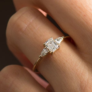 May include: A gold ring with a large emerald-cut diamond and two smaller pear-shaped diamonds on either side.