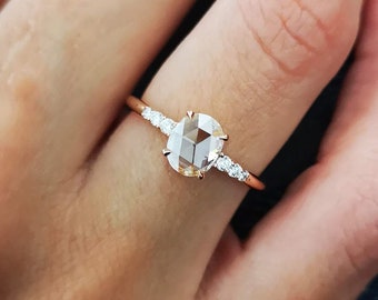 May include: A rose gold engagement ring with a large oval-shaped diamond and smaller diamonds set in a band.