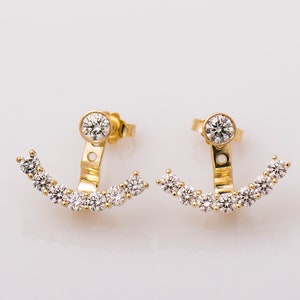 May include: A pair of gold earrings with a curved row of clear cubic zirconia stones. The earrings have a hinged design that allows them to be worn as a single stud or as a curved row of stones.