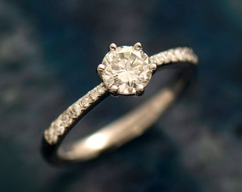 May include: A silver engagement ring with a single round diamond and a band of smaller diamonds.