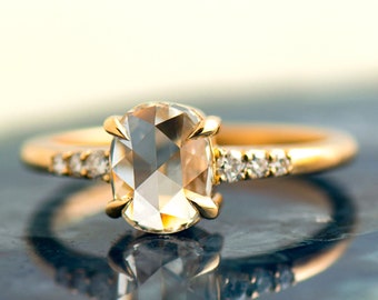 May include: A gold ring with a large, clear, faceted gemstone set in the center. The band is accented with smaller diamonds.