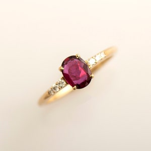 Può includere: Un anello d'oro con una pietra ovale rossa e piccoli diamanti incastonati nella fascia.