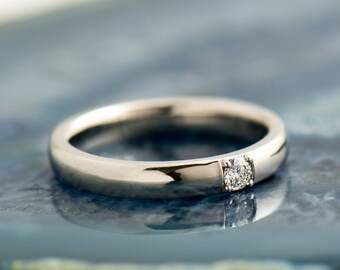 May include: A simple silver band with a single, small, round diamond set in the center.