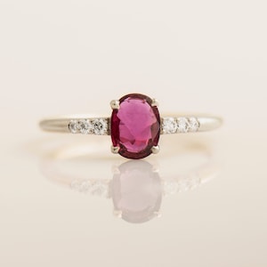 Può includere: Un anello d'argento con una pietra ovale rosa circondata da piccole pietre chiare.