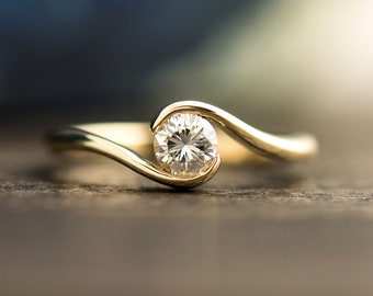 Op de afbeelding: Een gouden verlovingsring met een enkele ronde diamant gezet in een gebogen band.
