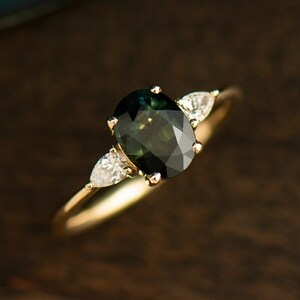 May include: A gold ring with a dark green oval gemstone and two smaller pear-shaped diamonds on either side.