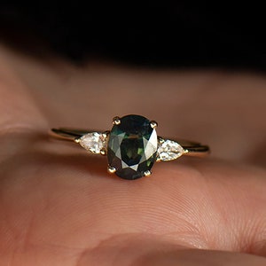 May include: A gold ring with a dark green oval gemstone and two smaller pear-shaped diamonds on either side.