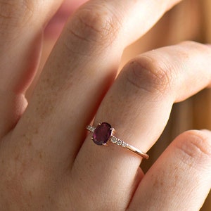 Può includere: Un anello in oro rosa con una grande pietra preziosa ovale di colore viola e pietre preziose più piccole e trasparenti sulla fascia.