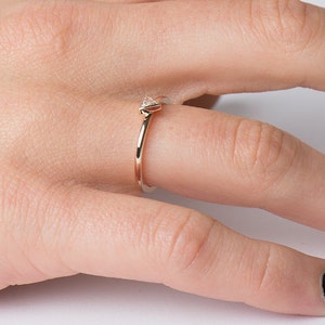 May include: A delicate gold ring with a small, triangular diamond set at the top. The ring is worn on a finger.