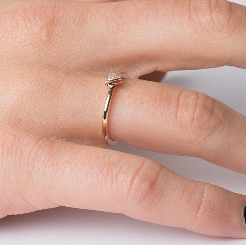 May include: A delicate gold ring with a small, triangular diamond set at the top. The ring is worn on a finger.