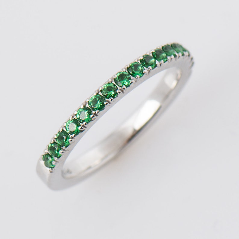 May include: A delicate silver band ring with a row of small, bright green gemstones.