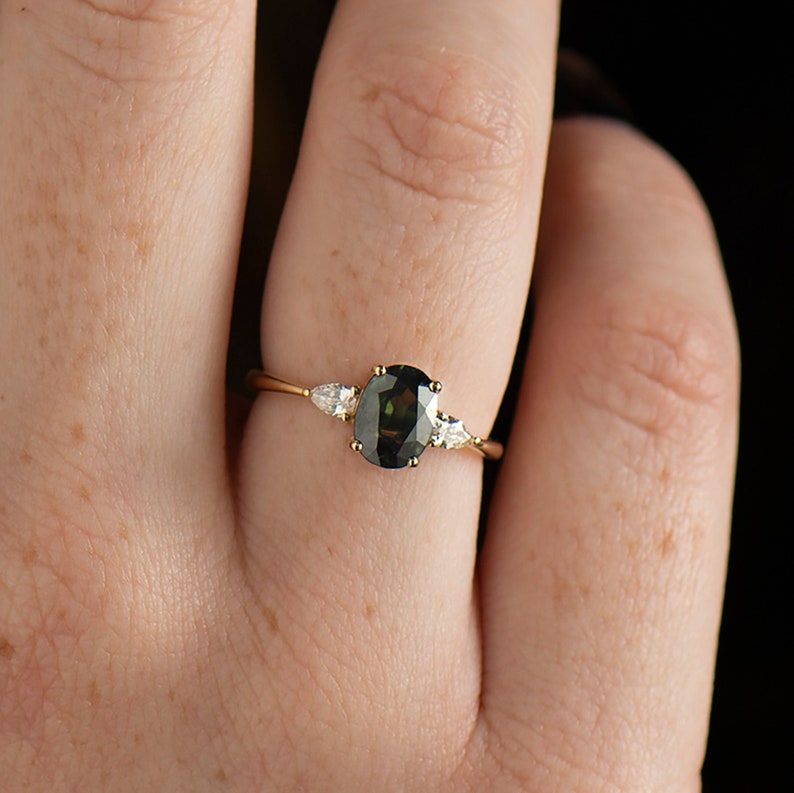 May include: A gold ring with a dark green oval gemstone and two smaller pear-shaped diamonds on either side.