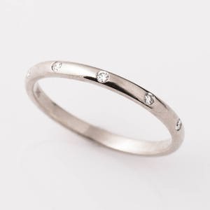 Könnte beinhalten: Ein dünner Silberring mit kleinen Diamanten, die in einer Reihe um den Ring herumgesetzt sind.