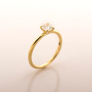 May include: A simple gold band engagement ring with a single round diamond.